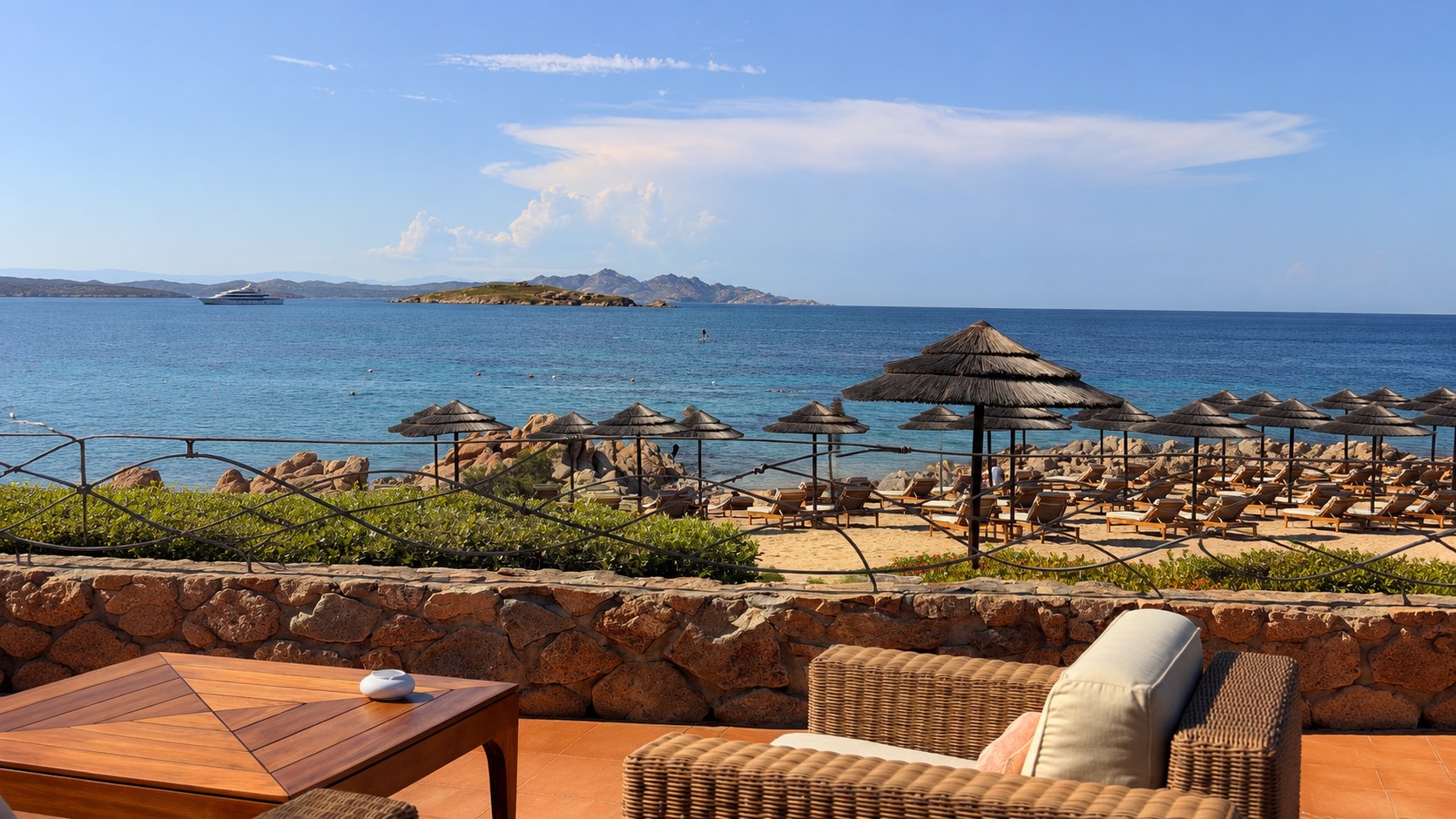 Beach club terrace overlooking a turquoise Mediterranean bay lined with thatched umbrellas