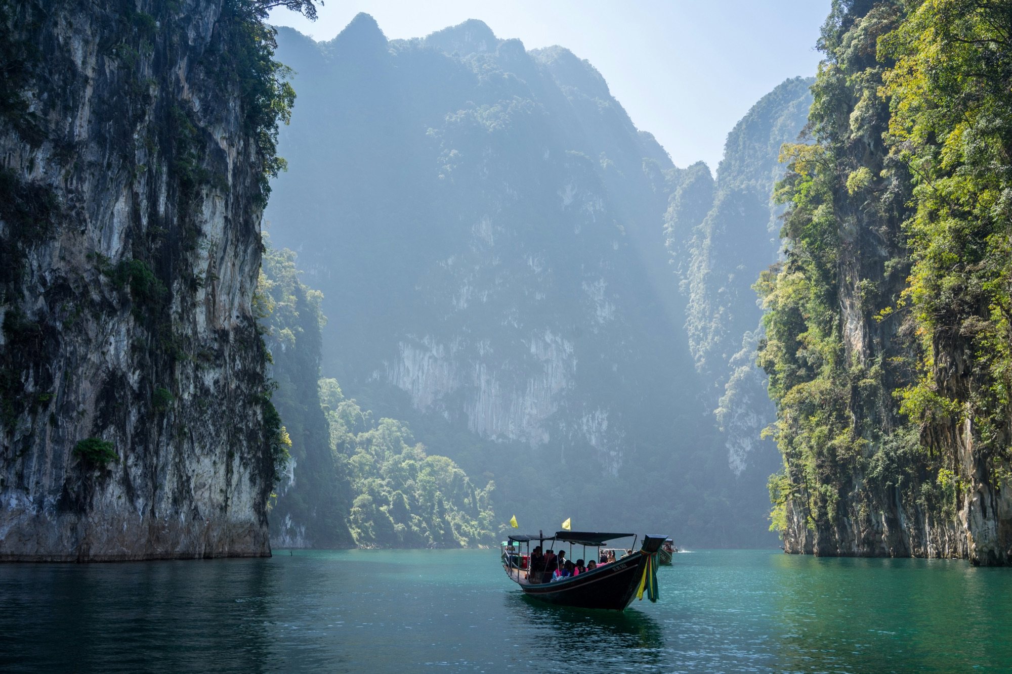 Longtail boat drifting between jungle-clad limestone cliffs in Thailand